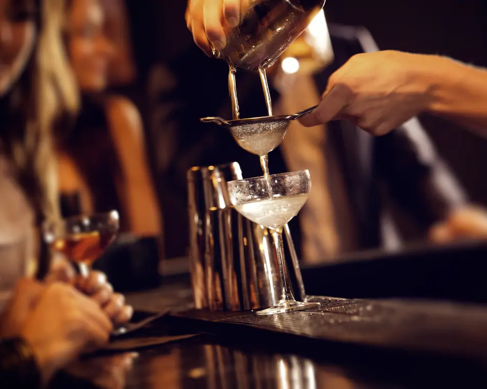 Bartender double-straining a cocktail into a coupe